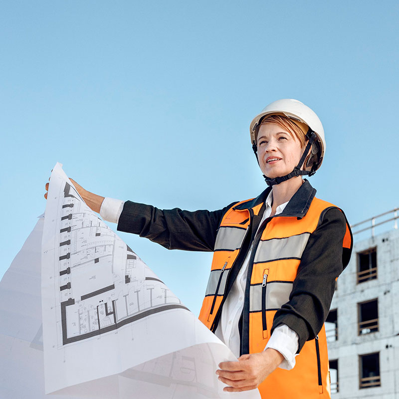 Rakennusmaan työntekijä pitelee suunnitelmapiirrosta kädessään ja katsoo ylös päin