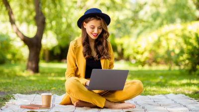 Nainen istuu puistossa ja lukee artikkelia tietokoneeltaan