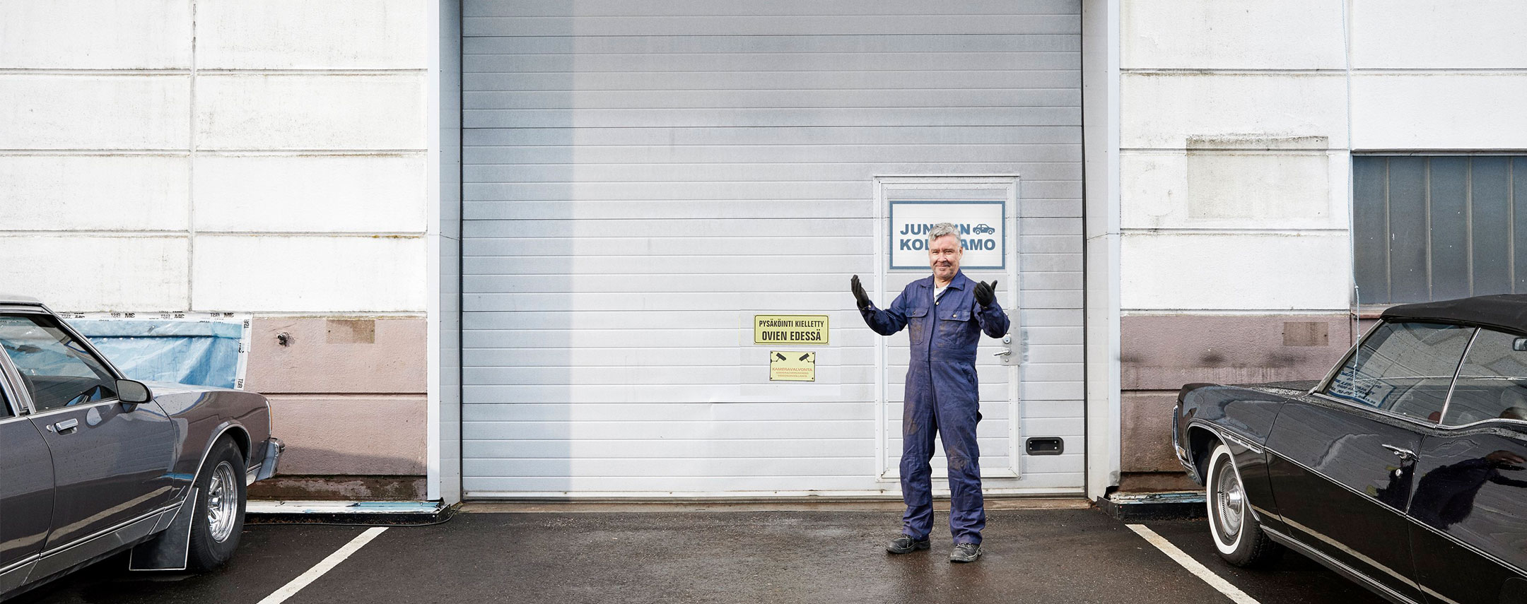 Yrittäjä seisoo tervehtien autokorjaamonsa pihalla